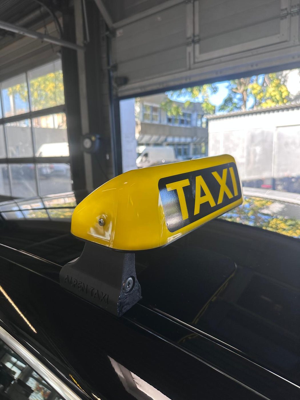 Gelbe Taxi-Dachleuchte auf einer schwarzen schwebenden Halterung mit eingeprägtem Schriftzug Alpen Taxi