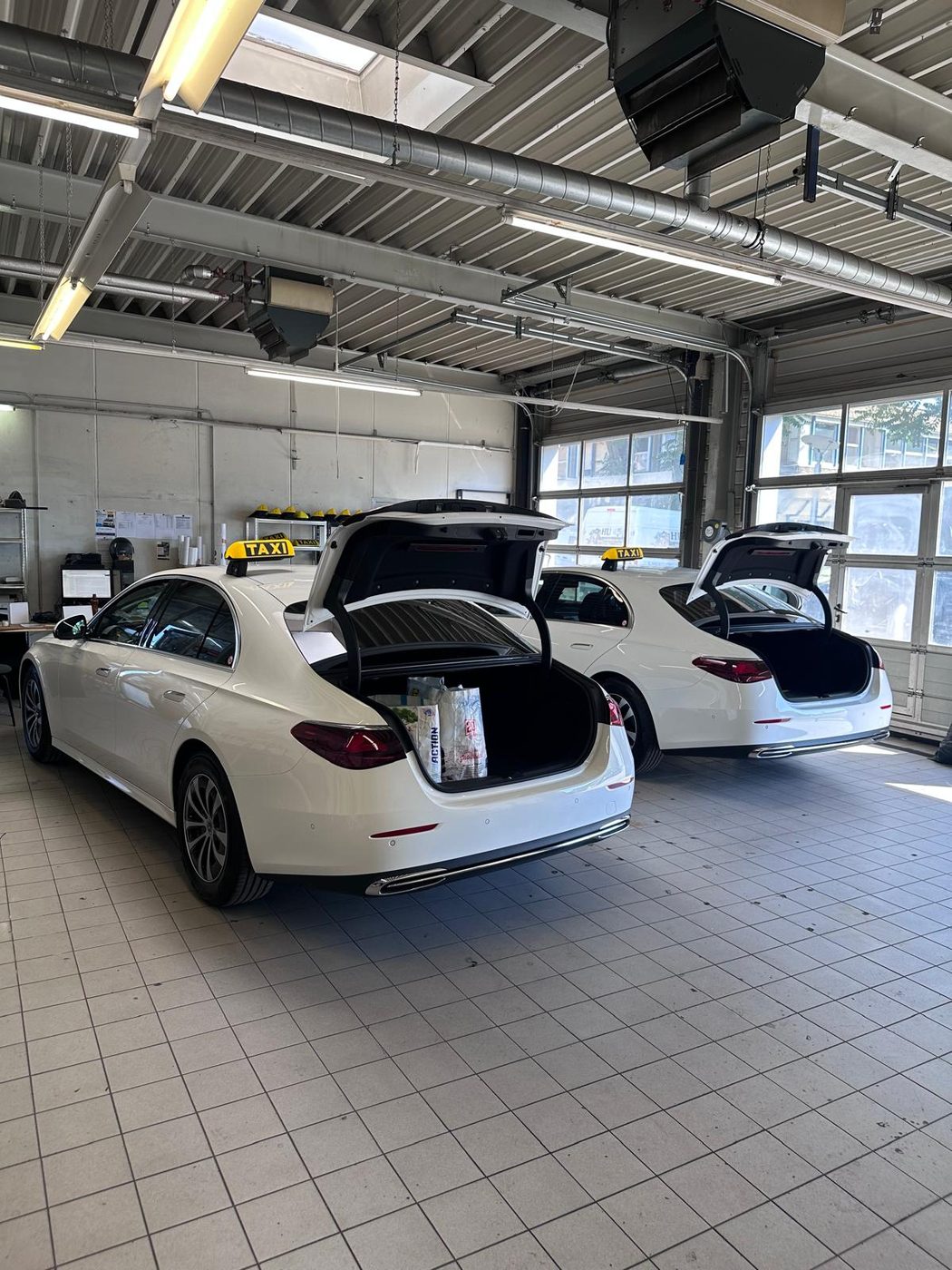 Zwei weiße Mercedes E-Klasse Taxis mit geöffneten Kofferräumen